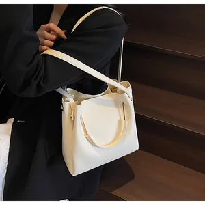 Borsa a secchiello bianco crema con manico a U dorato presentata su scale di legno