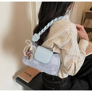 Detail of light blue crossbody bag with braided handle and decorative pearl charm