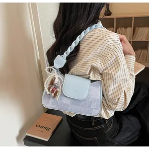 Detail of light blue denim patchwork bag with woven strap and decorative pearl charm