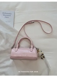Detail view of pink cylinder shoulder bag with plush ball charm on white fabric