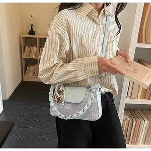 Detail of light blue plaid crossbody bag featuring a pearl bear charm and woven handle