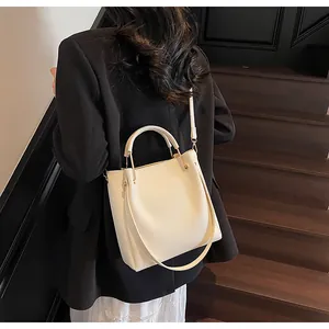 Dettaglio della borsa a secchiello bianco crema con finiture dorate e modella in blazer
