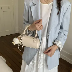 Chic beige cylindrical handbag with plush charm and beaded strap for daily use
