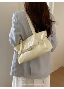 Detail of cream shoulder bag featuring polished leather texture and metal eyelet straps