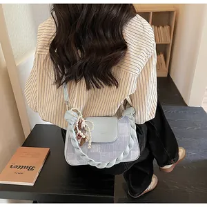 Detail of light blue denim handbag with braided shoulder strap and pearl charm