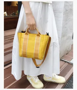 Detail of yellow canvas bucket bag with beige straps carried by a model in a white dress