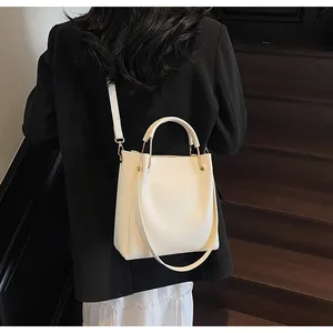 Dettaglio borsa a secchiello bianca con finiture dorate su una giacca blazer nera