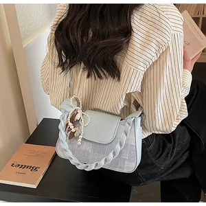 Detail of light blue crossbody bag with denim texture and pearl bow charm accessory