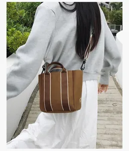 Detail of canvas bucket bag with brown vertical stripes and sun embroidery logo
