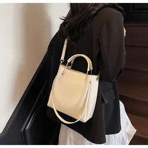 Borsa a secchiello beige con manico in metallo indossata a tracolla da una modella elegante
