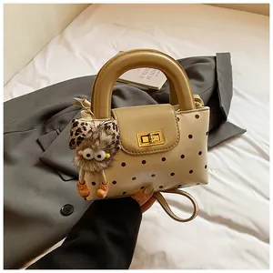 Detail der beigen Polka-Dot-Handtasche mit Goldschloss und Plüschmonster auf Blazer