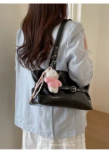Detail of black glossy leather tote bag with a plush bear charm and buckle straps
