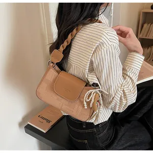 Detail of khaki shoulder bag with woven strap, pearl bow charm, and textured finish