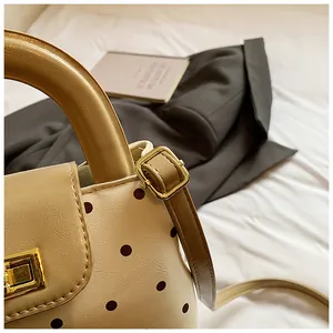 Detail der cremefarbenen Polka-Dot-Handtasche mit Lederstruktur und goldener Schnalle