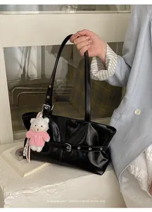 Detail of black glossy tote bag with silver buckles and a cute plush bear charm