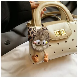 Detaillierte Ansicht einer cremefarbenen Handtasche mit Punkten und Monster-Anhänger