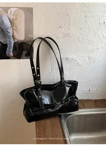 Detail of minimalist black patent leather tote with metallic eyelets and buckle straps