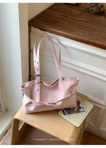 Detail showing pink glossy tote bag with adjustable metal buckle straps on a wooden bench