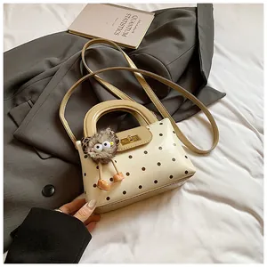 Detailansicht einer beigen gepunkteten Handtasche mit goldenem Drehverschluss auf Blazer