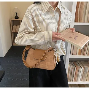 Close-up of beige textured crossbody bag with pearl charm and slim shoulder strap