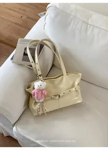 Close-up of cream retro tote bag with buckle strap on a white sofa with bear charm
