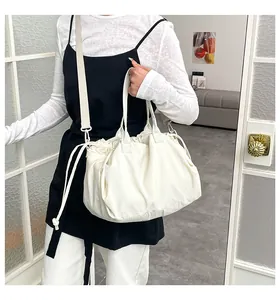 Detail view of model carrying white pleated cloud tote bag with thick strap in indoor setting