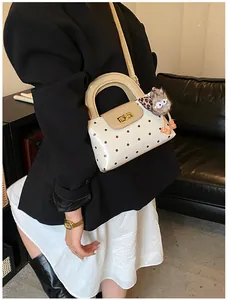 Detail der cremefarbenen Polka-Dot-Handtasche mit goldenem Drehverschluss und Plüschtier