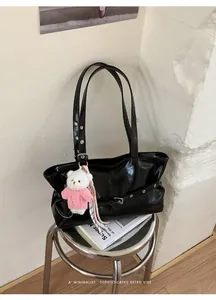 Detail of glossy black tote bag with long straps and a cute plush bear charm on a metal stool