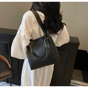 Dettaglio della borsa a secchiello in pelle nera con finiture dorate su abito bianco