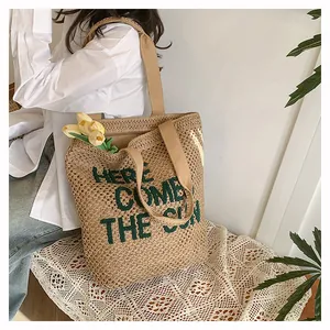 Detail of woven beach tote featuring Here Comes The Sun green embroidery and beige handles