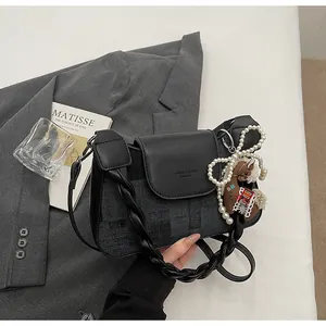 Detail of grey denim crossbody bag with black leather flap and pearl horse charm
