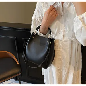 Dettaglio di una borsa a secchiello nera con manico ad anello dorato tenuta da una modella