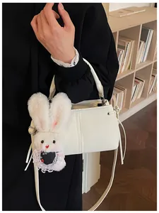 Detail of white soft leather handbag with cute plush bunny charm on a wooden shelf