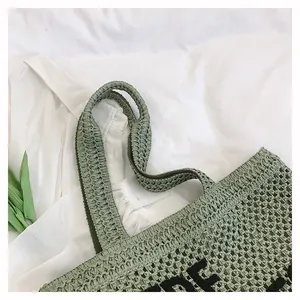 Close-up of light green woven tote bag with black letter crochet and wide handles