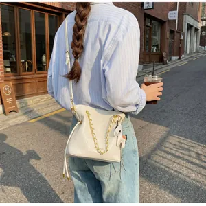 Outdoor street view of a white quilted chain bucket bag with a colorful pony charm