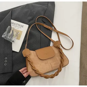 Detail of earthy brown crossbody bag showing woven texture handle and flap branding