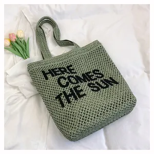 Detail of green knit tote bag with black 'HERE COMES THE SUN' text and hollow mesh texture