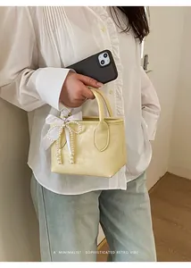 Dettaglio borsa a mano gialla minimalista con ciondolo a fiocco in raso e perle