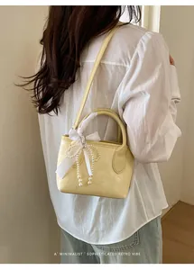 Dettaglio di una borsa a secchiello giallo tenue con fiocco di perle e sciarpa di seta