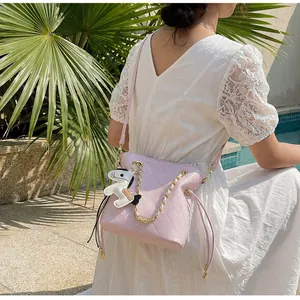 Quilted pink bucket bag with gold chain strap and horse charm shown in an outdoor setting