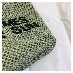 Close-up of green woven straw bag featuring hollow mesh pattern and black SUN embroidery
