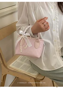 Dettaglio borsa a secchiello rosa chiaro con manico in nastro di raso e fiocco di perle