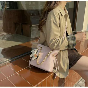Detail of pink quilted bucket bag with chain strap and horse charm worn with beige coat