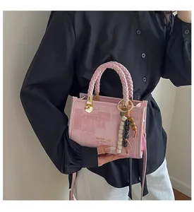 Détail d'un sac à bandoulière rose texturé avec pendentif perles et lettrage doré