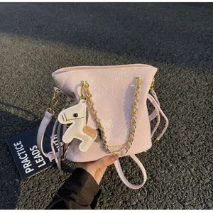 Detail of pink quilted bucket bag with chain strap, fringe, and cartoon horse charm