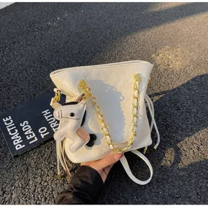 Detail of white quilted bucket bag featuring gold chain and a horse charm on a dark background