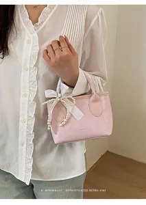 Dettaglio borsa a secchiello in pelle rosa con eleganti perle e fiocco sul manico