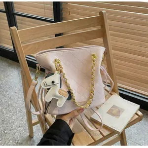 Detail of pink quilted bucket bag with gold chain and horse charm on wooden chair