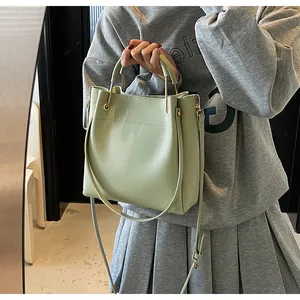 Dettaglio della borsa a secchiello verde chiaro con finiture dorate e tracolla su modella