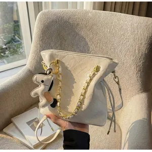 Detail of beige quilted bucket bag with golden chain handle and pony charm on a soft sofa